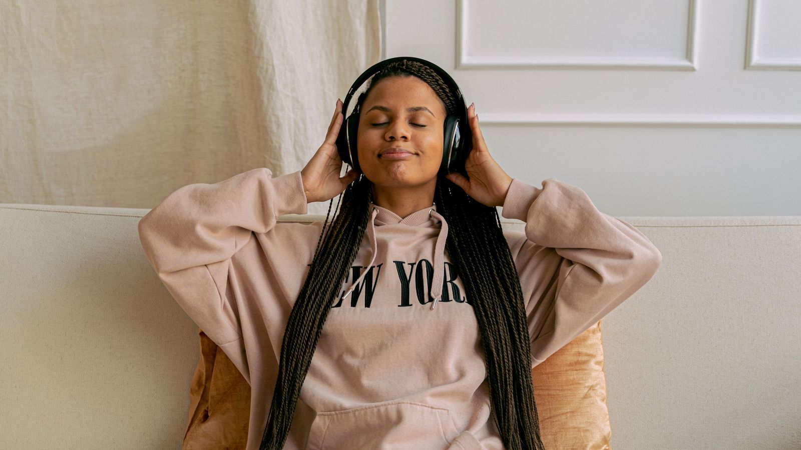A woman on a sofa listening through headphones with her eyes closed