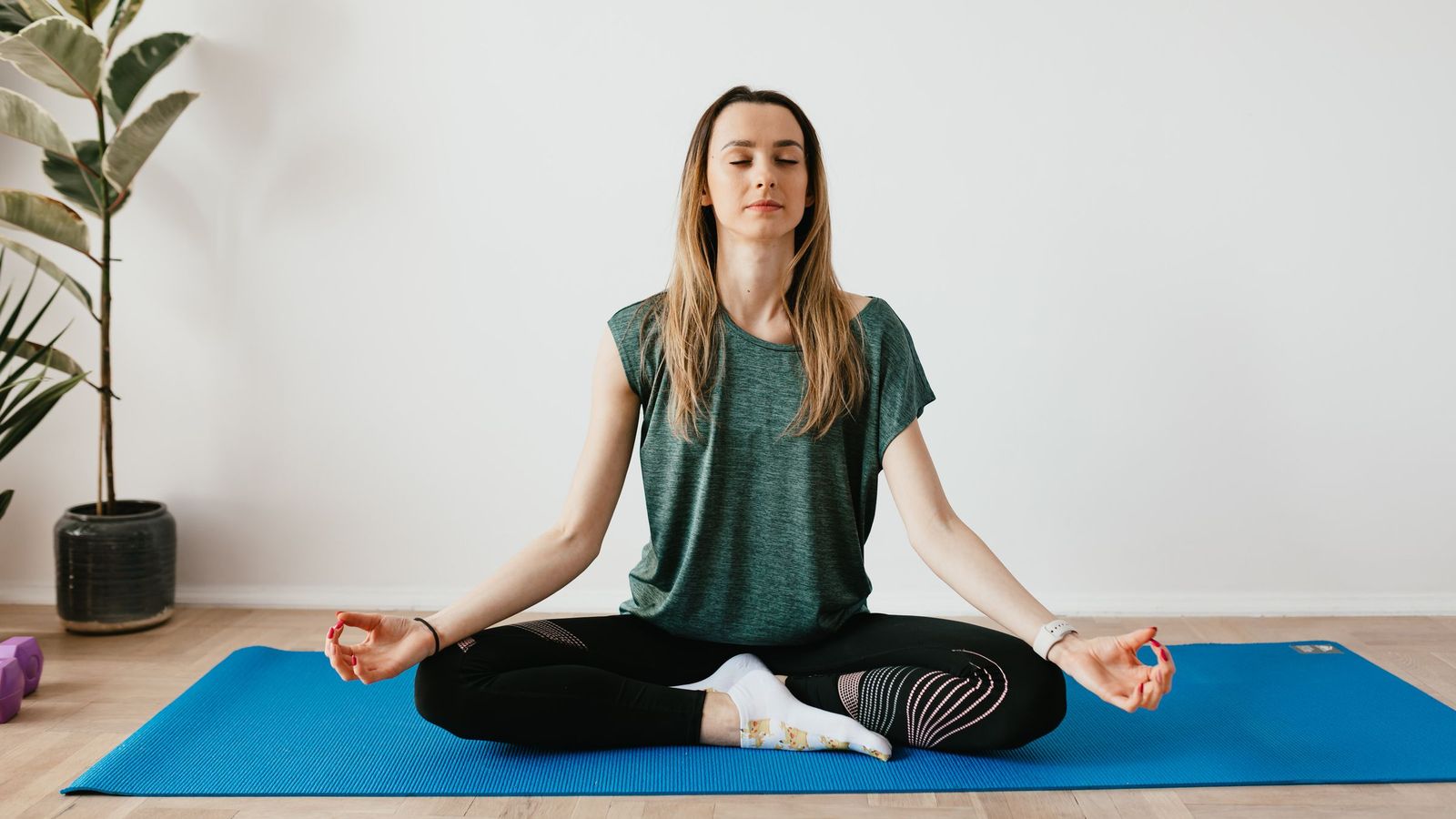 A woman meditating cross-legged on a mat at home