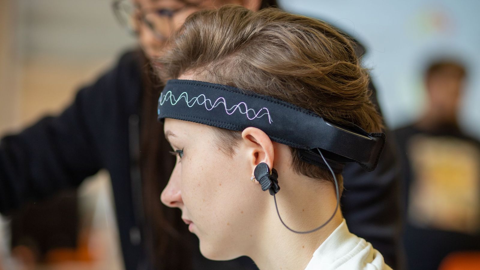A young woman wearing an EEG headband with an ear clip