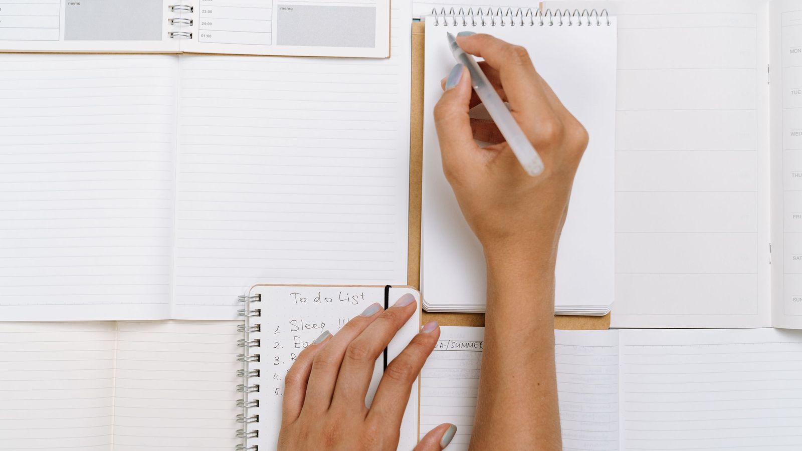 Two hands writing notes across several open notebooks