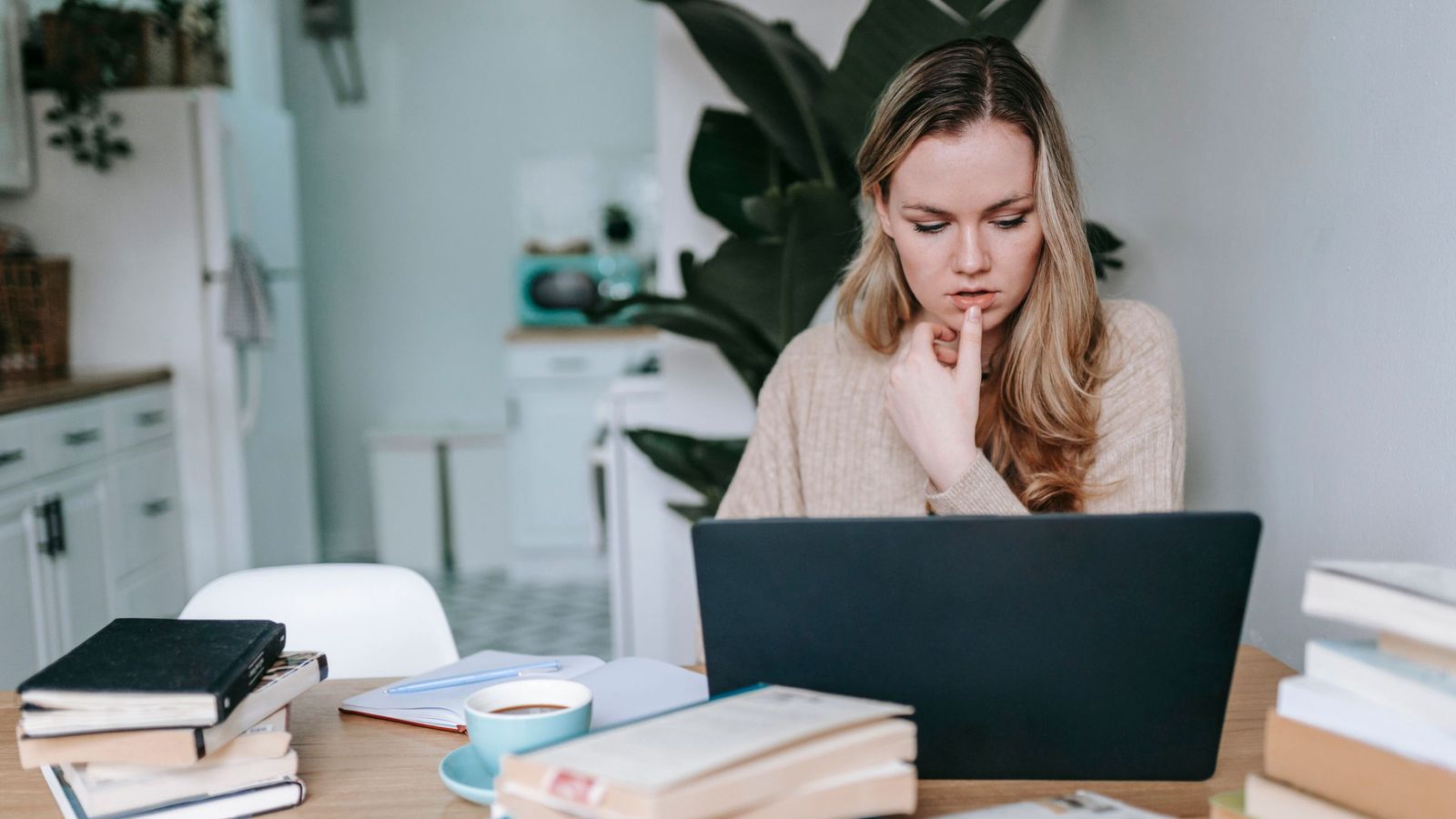 A woman thinking at a laptop, surrounded by books