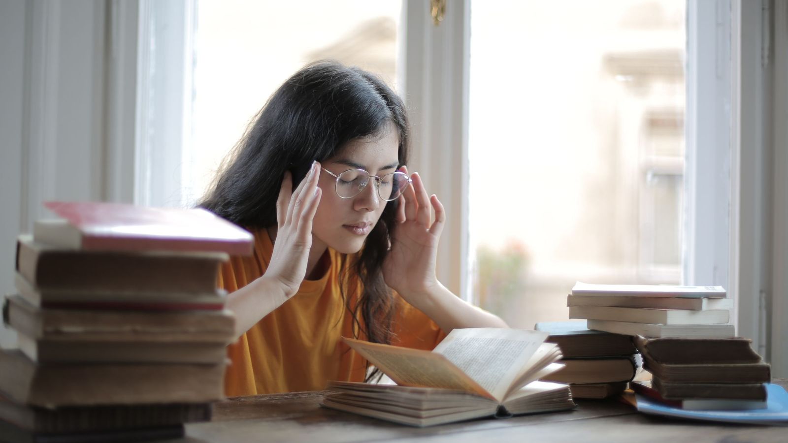 A student with her hands at her temples beside stacks of books