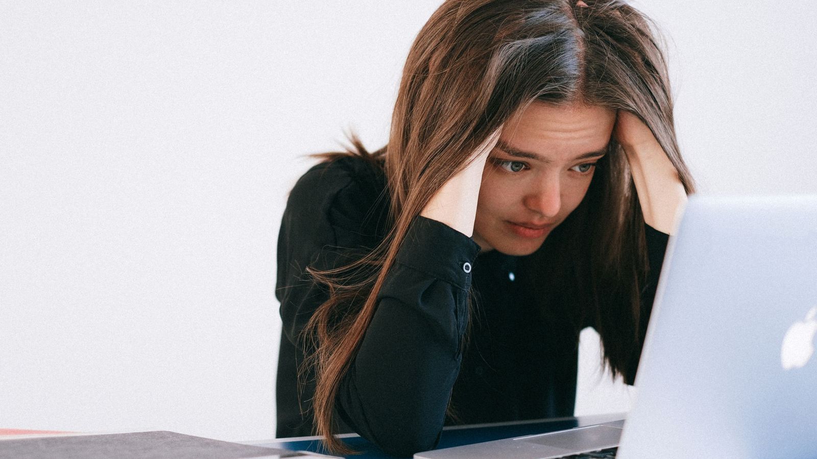 A woman holding her head while looking at a laptop