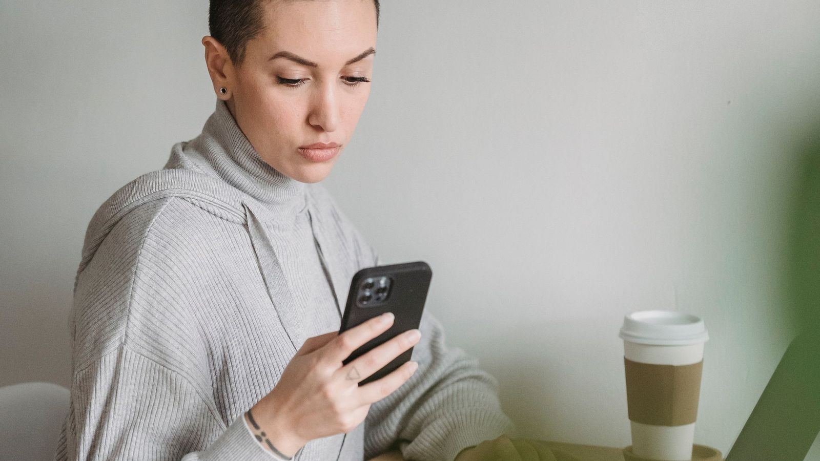 A woman looking at her phone at a desk with a coffee cup